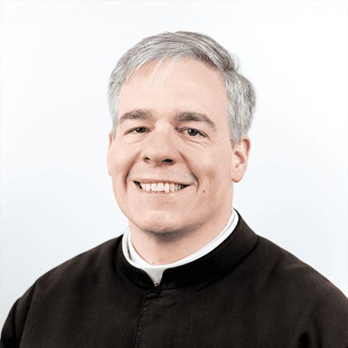 A priest in a green cassock smiling
